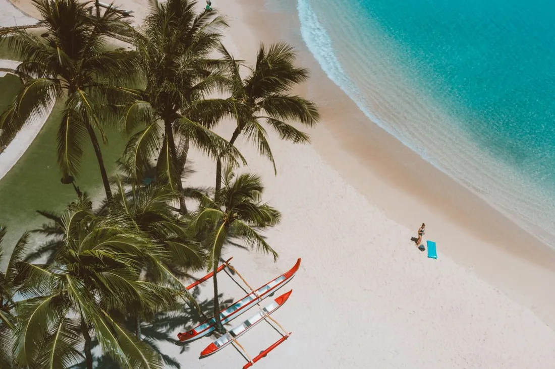 Palm trees over a white-sand Maui beach with an outrigger canoe and turquoise water